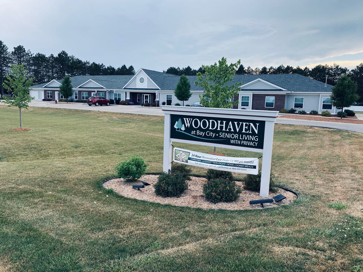 A sign for Woodhaven, in front of residential buildings under a cloudy sky.