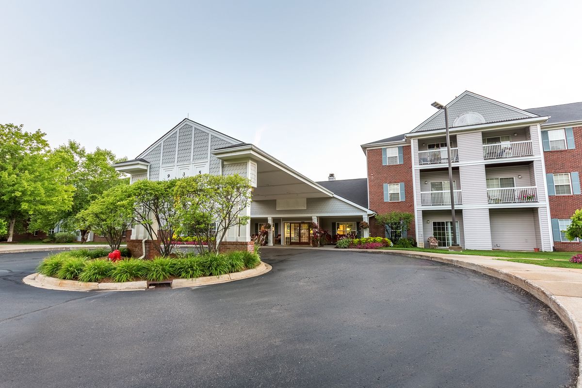 A view of a building entrance with a landscaped driveway and surrounding greenery.