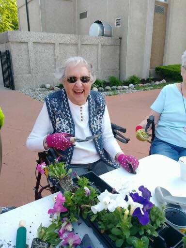 Elderly woman smiling in her wheelchair while enjoying the outdoors with friends.