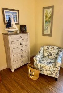 A cozy corner with a nautical-themed chair and dresser, featuring a model ship and framed artwork.