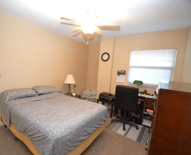 A cozy bedroom with a bed, desk, and ceiling fan.