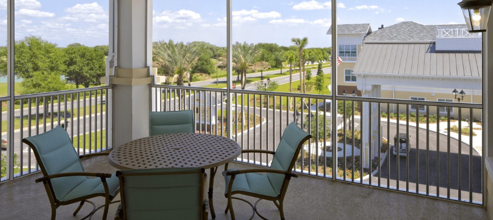 A cozy balcony with a table and chairs overlooking a scenic, tree-lined residential area.