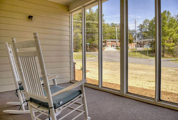 A cozy porch with a rocking chair and large windows offering a view outside.