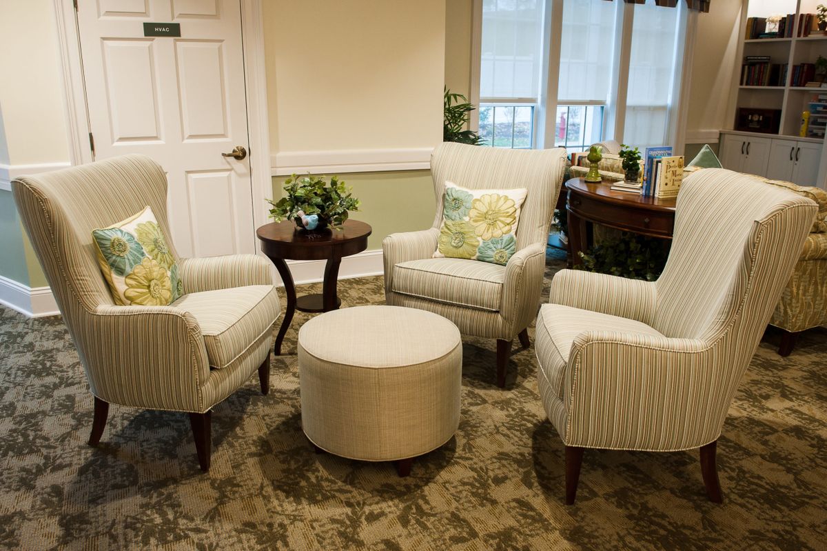 A cozy seating area featuring three armchairs, an ottoman, and a small round table with plants and decorative pillows.