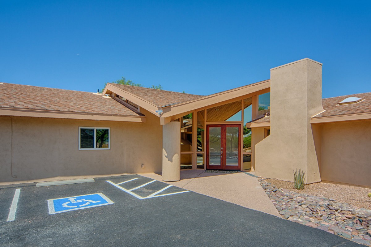 A modern house with a large entrance, set in a desert landscape under a clear blue sky.