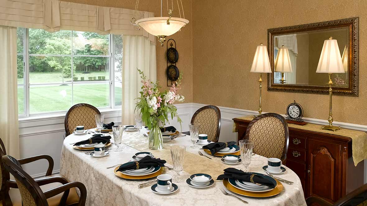 A beautifully arranged formal dining table with elegant place settings and a central flower arrangement in a well-decorated dining room.