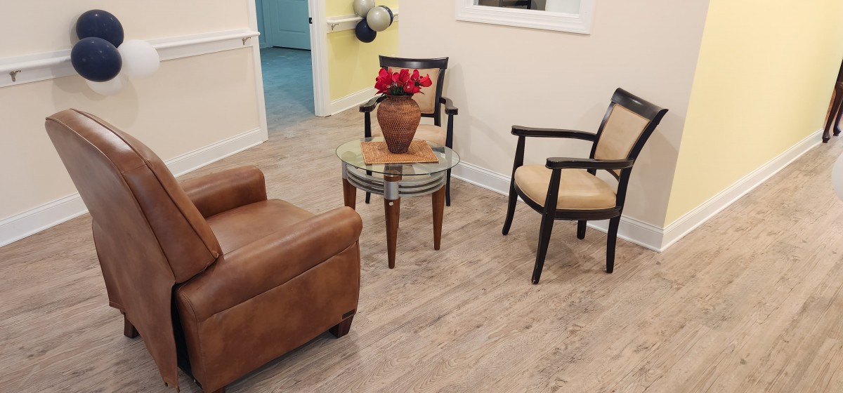 A cozy waiting area featuring two chairs, an armchair, and a small table with a vase of red flowers.