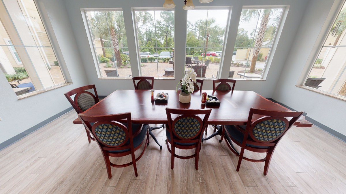 A dining area with a wooden table surrounded by chairs, featuring large windows that let in ample natural light.
