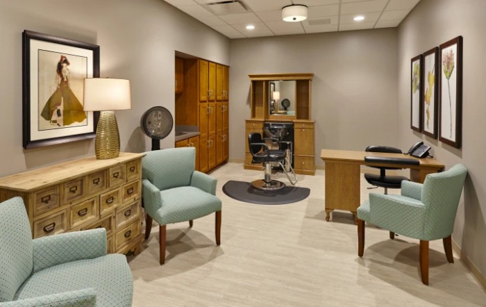 A modern salon interior featuring comfortable chairs, a styling station with mirrors, and warm lighting.