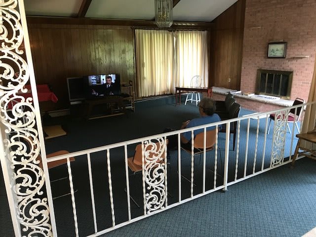A cozy living room with wood paneling and a carpeted floor, featuring a TV and a fireplace.