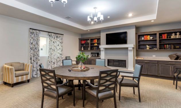 A modern living room with a round table and chairs, featuring a fireplace and a mounted television.