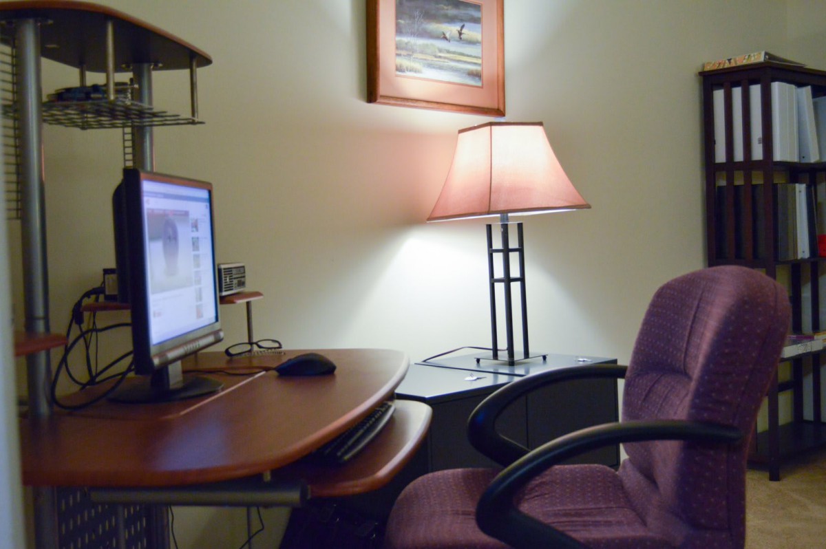 A cozy office space with a computer desk, monitor, and lamp.