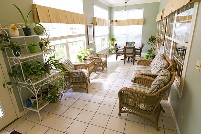 A bright sunroom with wicker furniture and lush indoor plants.