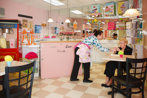 A cozy dessert shop with a waitress serving a customer in a vibrant pink-themed interior.