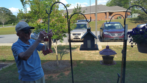 A person refilling a hummingbird feeder in their yard on a sunny day.
