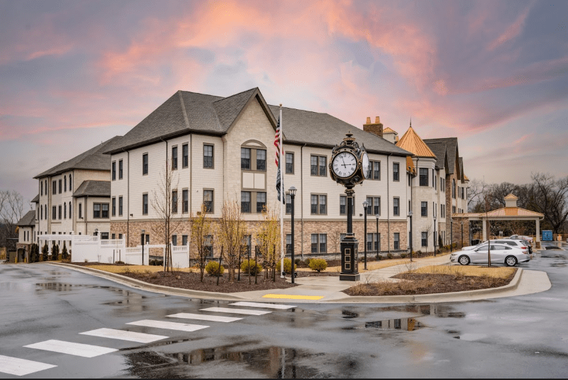 A residential building with a prominent clock tower stands at the intersection during sunset, reflecting on the wet pavement.