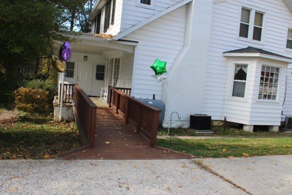 A white house with a wooden ramp leading to the entrance, adorned with colorful balloons.