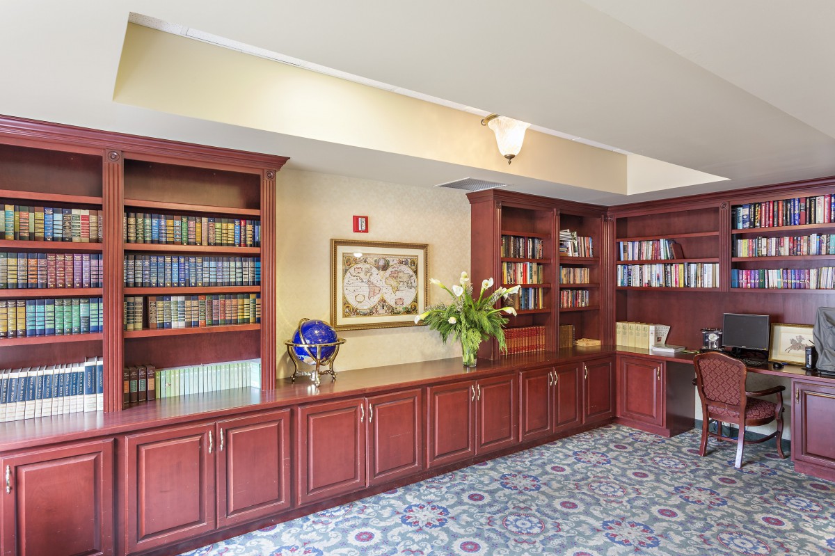 A cozy library corner with wooden bookshelves filled with books, a vase of flowers, and decorative items on the cabinets.