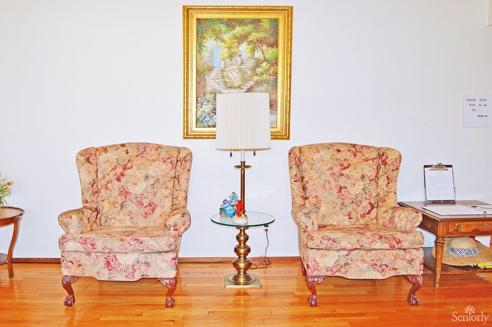 A cozy living room setup with two floral armchairs and a glass-top side table adorned with a lamp and decorative items.