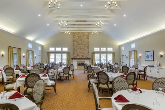 A spacious and elegantly decorated dining room with neatly arranged tables and chairs, featuring a grand fireplace and large windows.