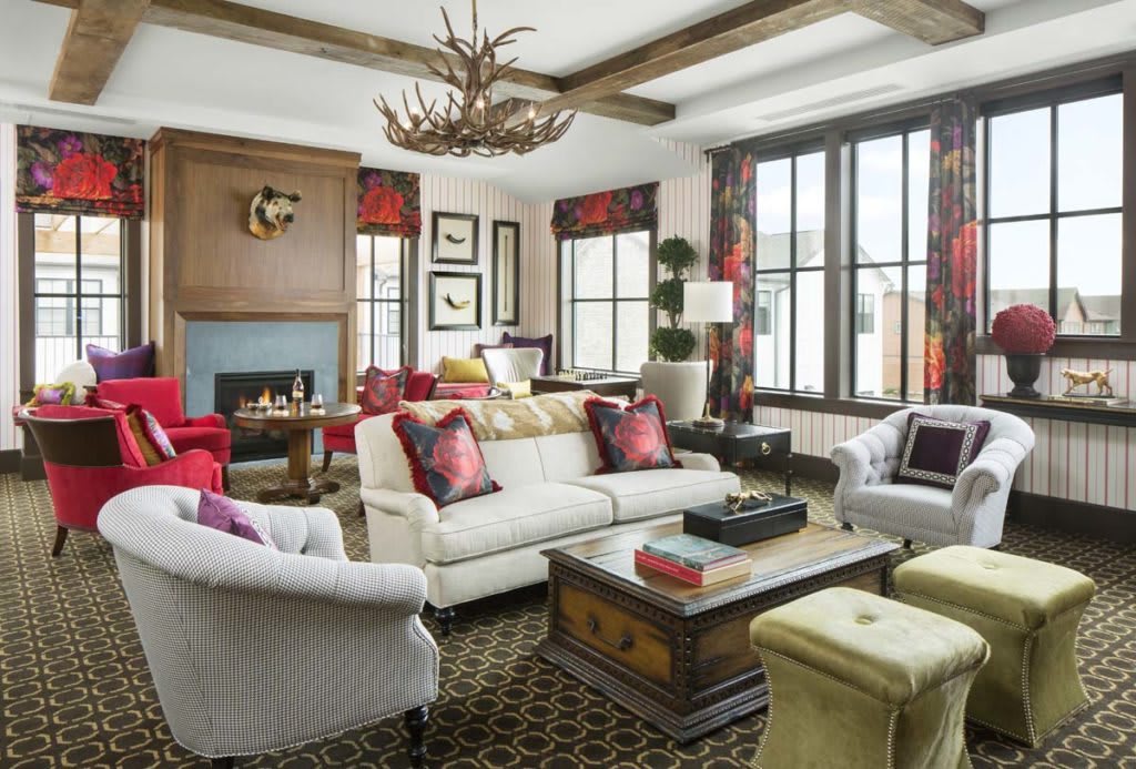 A stylish living room with elegant furniture and decor, featuring a central fireplace and antler chandelier.