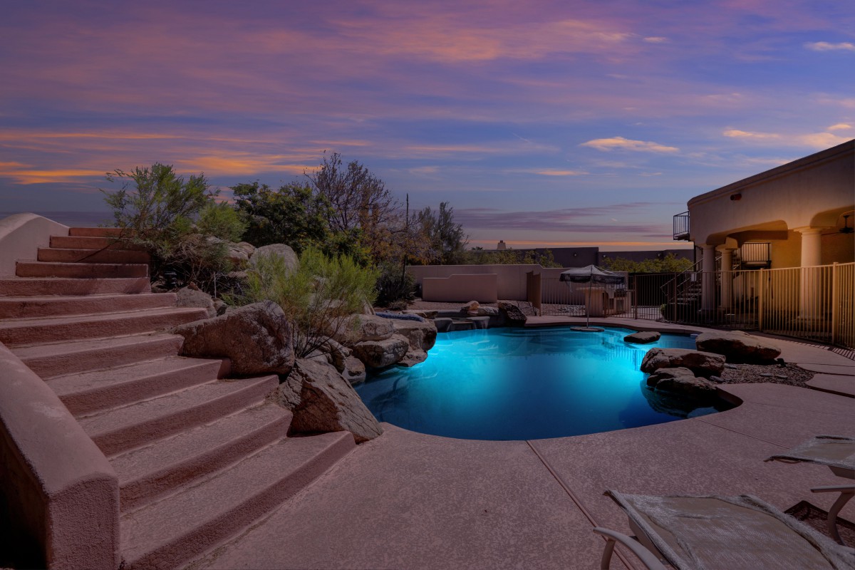 A beautifully lit backyard pool at dusk with stairs leading down to the water.