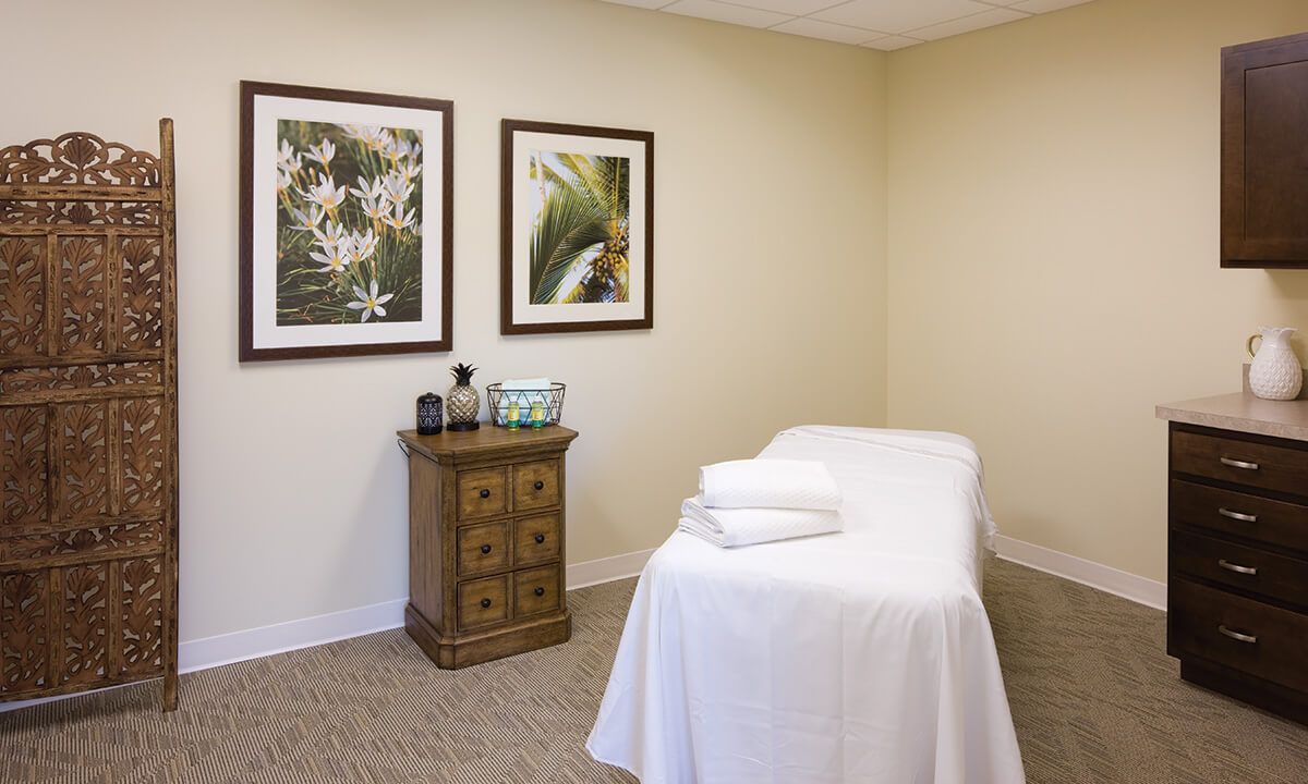 A serene massage room with a white treatment bed and calming decor.