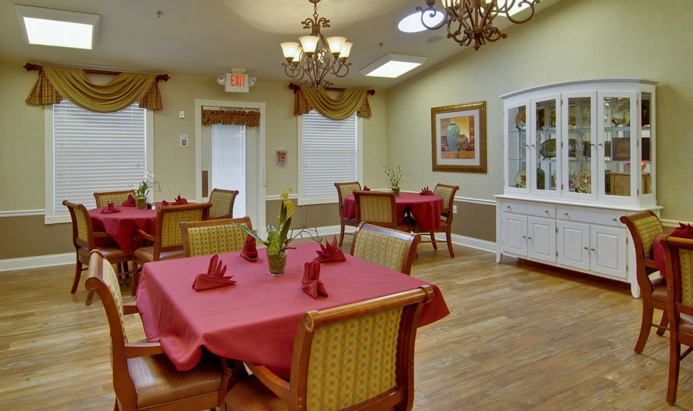 A cozy dining room with tables covered in red tablecloths and elegant chandeliers hanging from the ceiling.