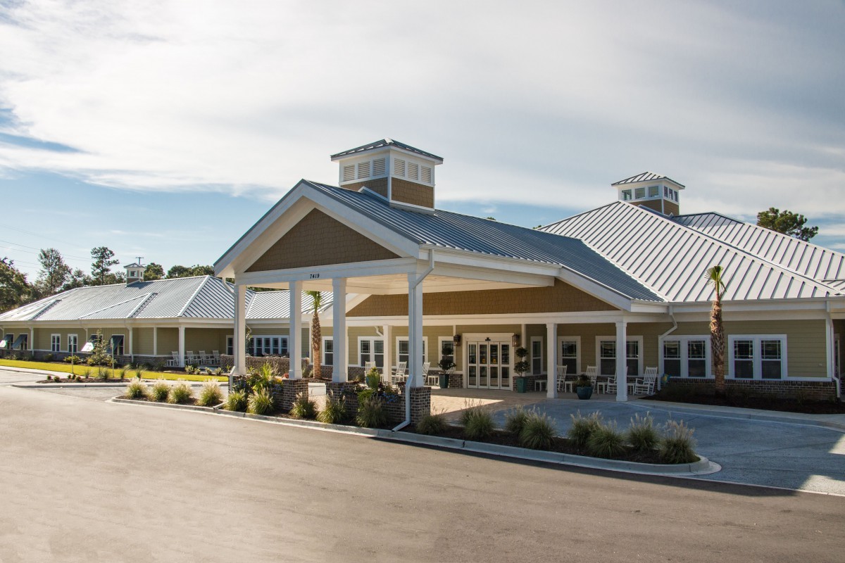 A modern building with a prominent entrance and landscaped surroundings under a clear sky.