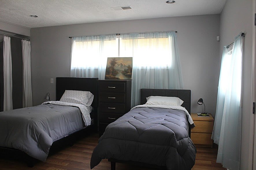 A bedroom with two single beds, a dresser, and a nightstand against light grey walls.