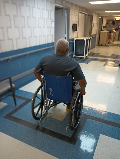 An elderly person in a wheelchair navigating through a hospital corridor.