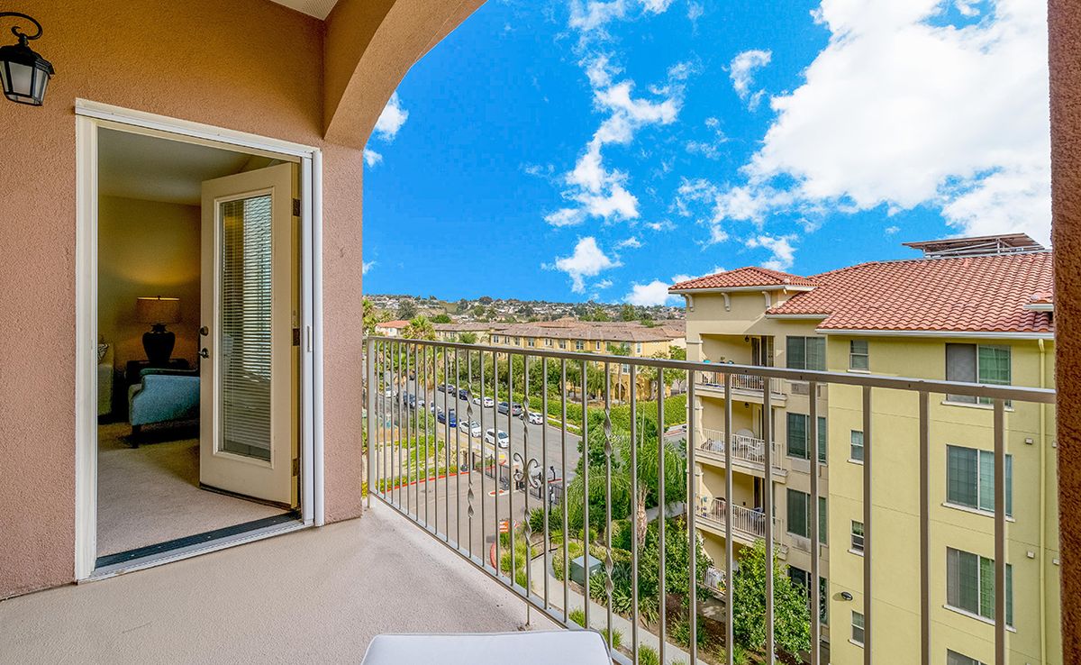 A scenic view from a balcony overlooking nearby buildings under a bright blue sky with clouds.