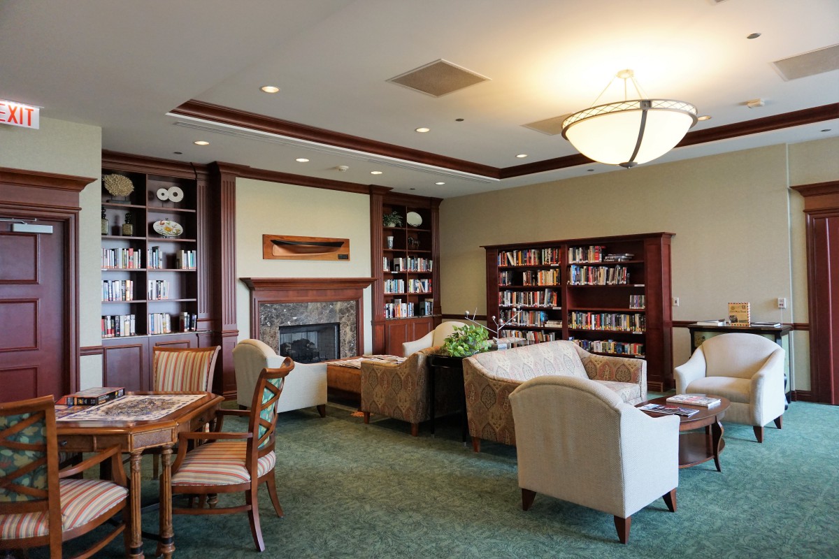 A cozy library lounge with bookshelves, armchairs, and a fireplace.