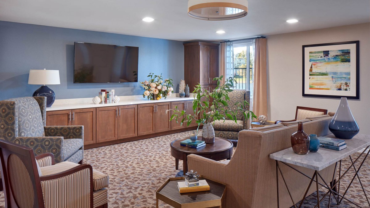 A cozy living room with modern furniture and a large television, accented by indoor plants.