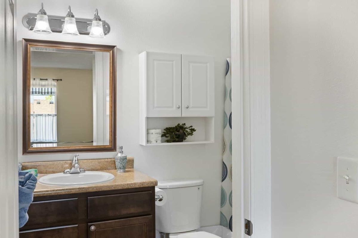 A modern bathroom with a sink, mirror, and cabinet above the toilet, featuring bright lighting.