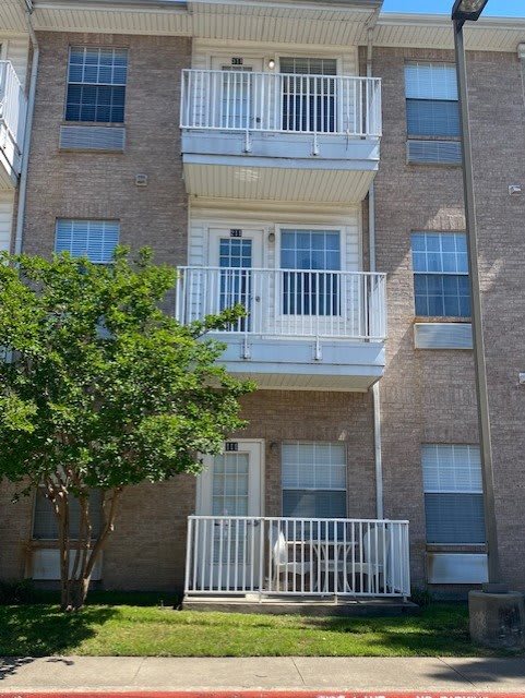 A residential apartment building with multiple balconies and a tree in front.