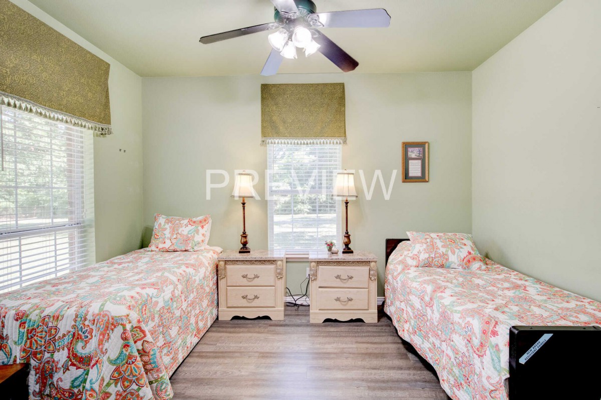 A cozy bedroom with twin beds and floral bedding, featuring matching nightstands and a ceiling fan.