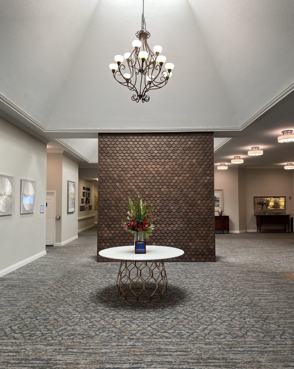 A modern lobby featuring a chandelier, a round table with a flower arrangement, and a prominent brick wall.