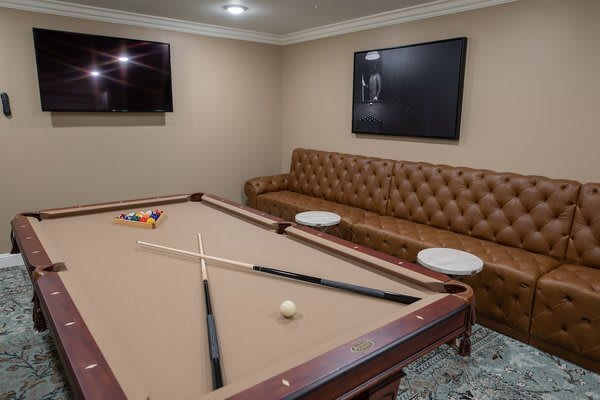 A cozy game room featuring a pool table, leather sofa, and wall-mounted television.