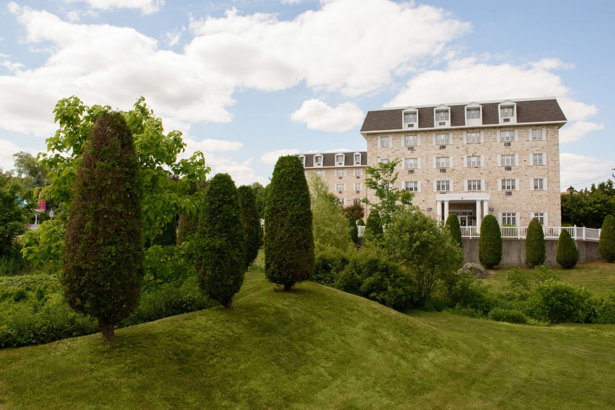 A scenic view of a historic building surrounded by manicured gardens and lush greenery under a partly cloudy sky.