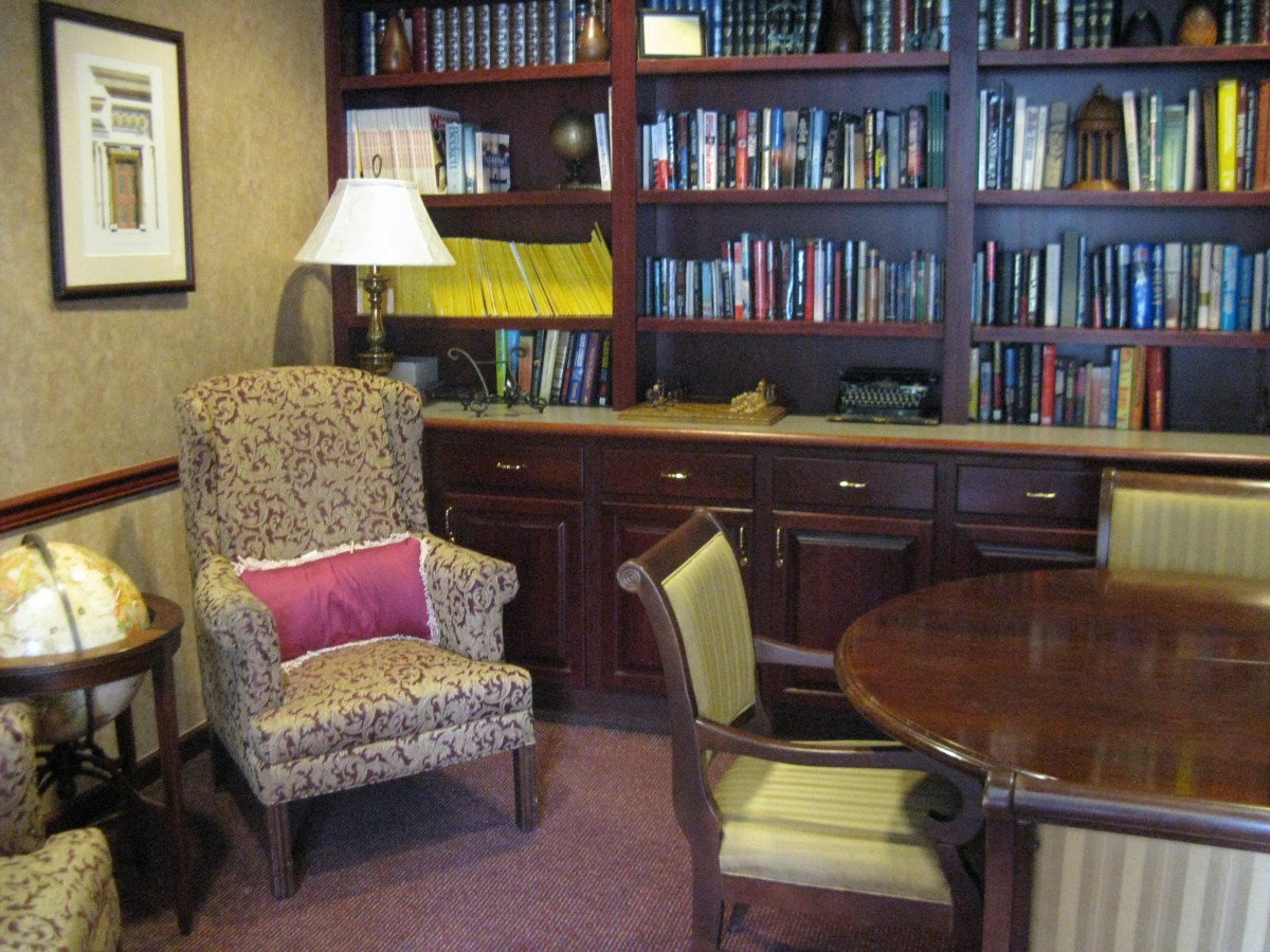 A cozy office library with a bookshelf, armchair, and table.