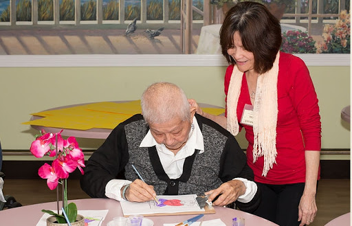 An elderly person engaged in painting with the assistance of a caregiver.