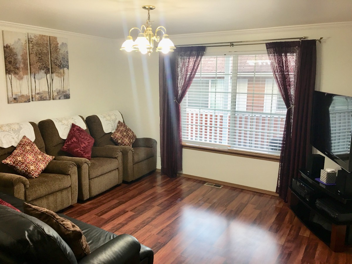 A cozy living room with hardwood floors, comfortable sofas, and a large window with curtains.
