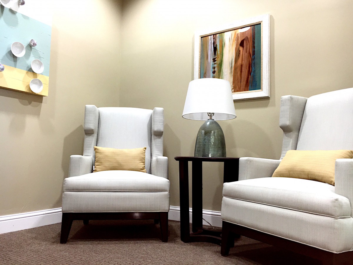 A modern living room setup with two white chairs, a central lamp, and abstract artwork on the wall.