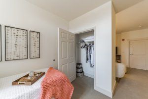 A minimalist bedroom featuring an open closet and a cozy bed with a coral blanket.