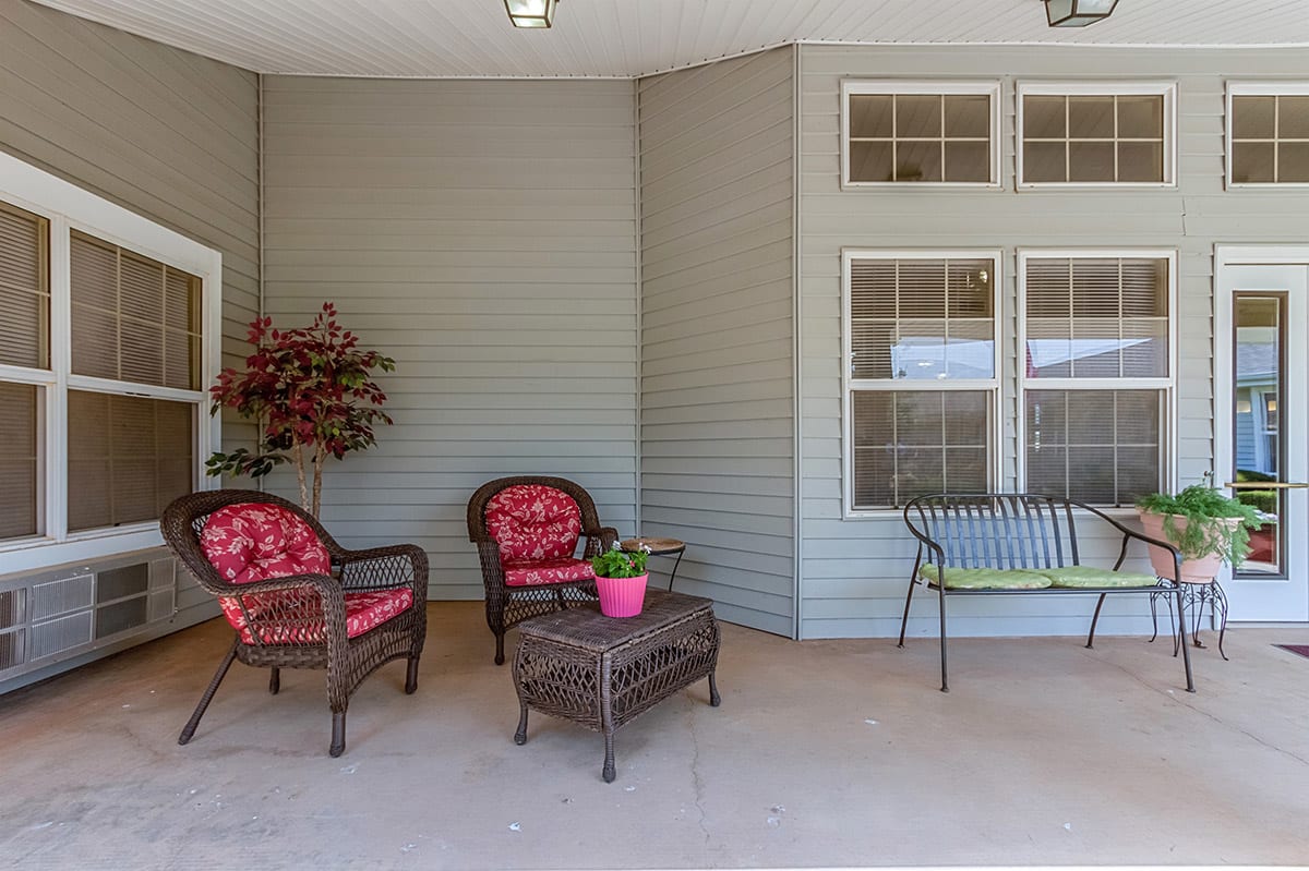 A cozy patio with wicker chairs and a table, accented by vibrant cushions and a potted plant.