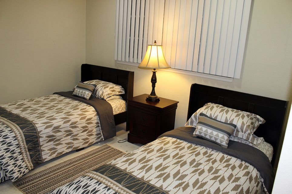 A cozy bedroom with two neatly made twin beds and a warm lamp on the nightstand.