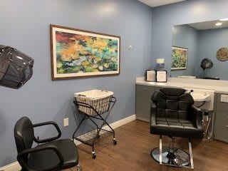 A cozy hair salon with stylish chairs, a large mirror, and vibrant artwork on the wall.