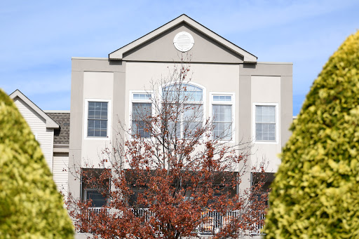 A residential building with large windows framed by a tree in autumn.