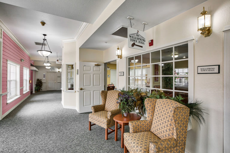 A cozy lobby area with patterned chairs, plants, and large windows.